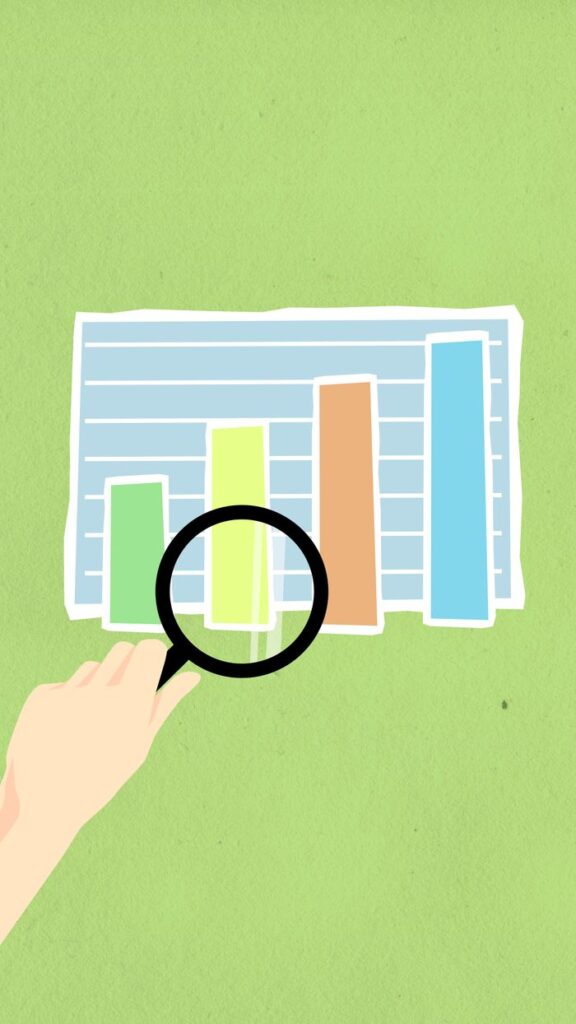 Top view of decorative cardboard illustration of hand with magnifying glass above diagram with columns on green background